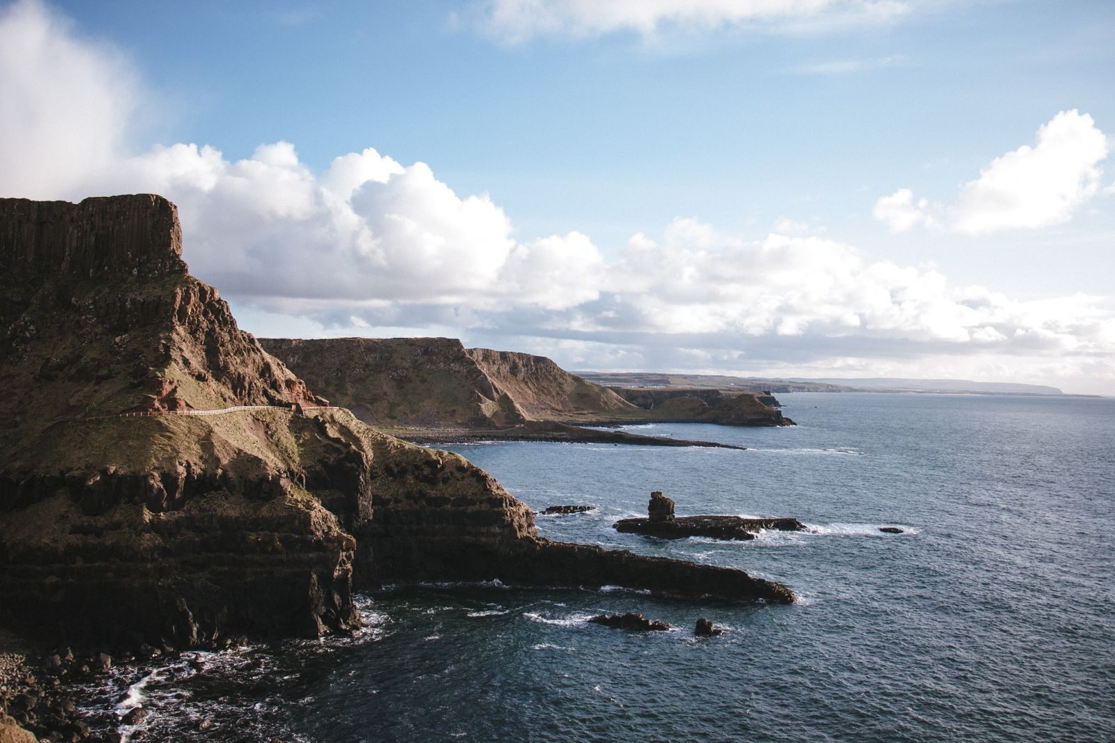 Picturesque scenery of rough rocky cliffs washed by calm majestic sea against cloudy blue sky
